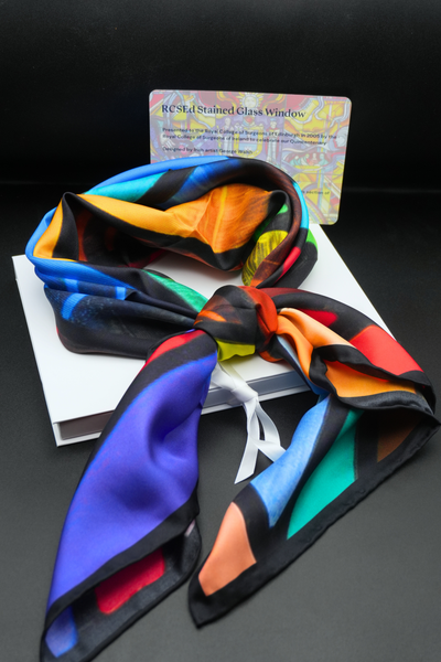 Image of the stained glass scarf tied in a knot with the box and postcard